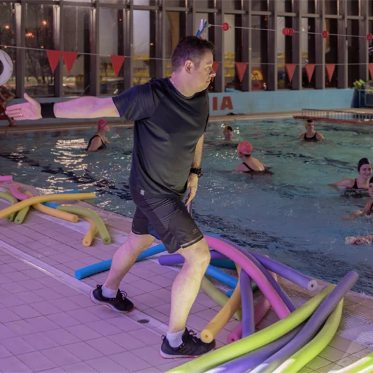 Fizjoterapeuta stoi na basenie i pokazuje ćwiczenia aqua fitness.