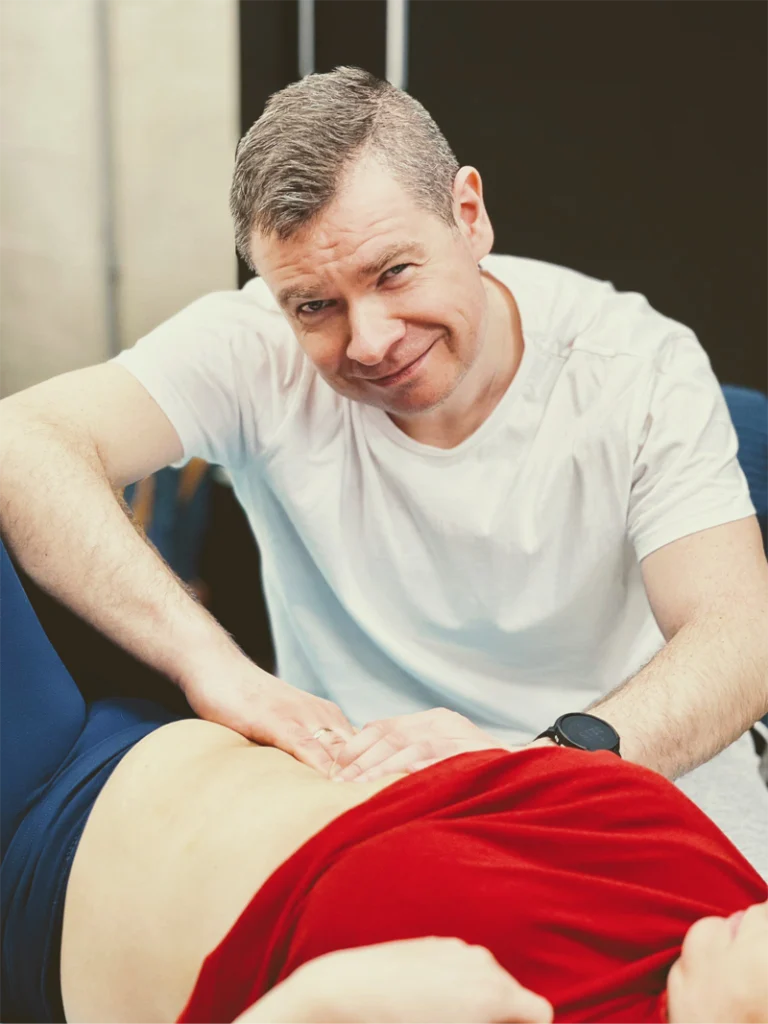 Fizjoterapeuta masuje kobietę po brzuchu, kiedy ona leży.