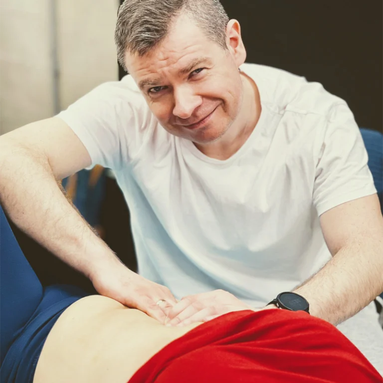 Fizjoterapeuta masuje kobietę po brzuchu, kiedy ona leży.