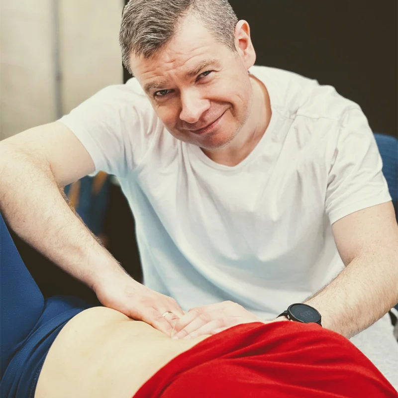 Fizjoterapeuta masuje kobietę po brzuchu, kiedy ona leży.